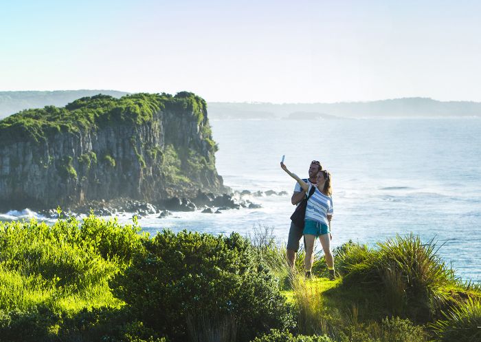 Couple taking photos on the scenic Minnamurra Headland overlooking Rangoon Island, Kiama Coast Walk in Kiama, South Coast